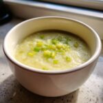 A close-up of a bowl of creamy potato leek soup topped with chopped green leeks.