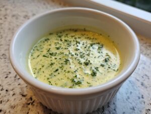 Close-up of creamy potato leek soup garnished with fresh green herbs in a white fluted bowl.