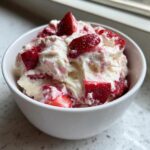 A close-up of creamy strawberry cheesecake dip mixed with chunks of fresh strawberries in a white bowl.