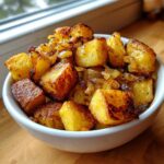 A white bowl filled with golden brown, crispy fried potatoes mixed with caramelized onions.