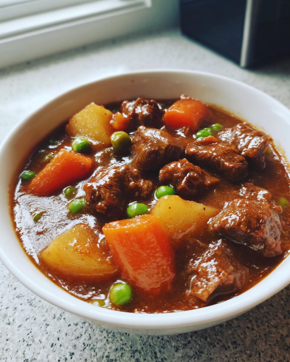 Close-up of a bowl filled with rich, thick crockpot beef stew featuring tender beef chunks, carrots, potatoes, and peas.