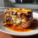 A close-up of a slice of moist crockpot french onion meatloaf topped with rich caramelized onions and melted Swiss cheese.