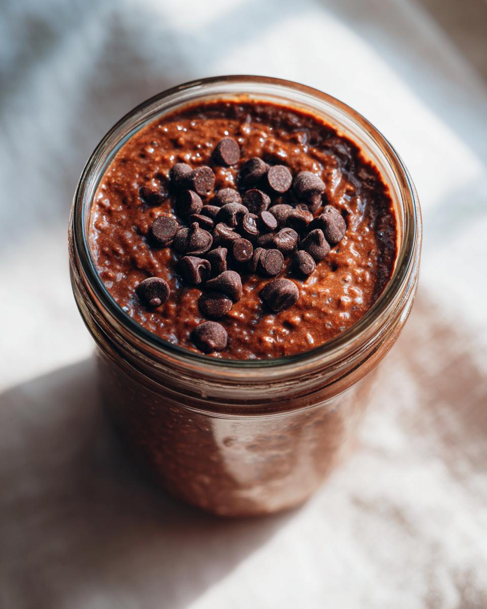 Overhead close-up of rich chocolate overnight oats in a glass jar, topped with dark chocolate chips.