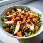 Close-up of a vibrant fall harvest salad featuring roasted butternut squash, apple slices, walnuts, and dried cranberries over mixed greens.