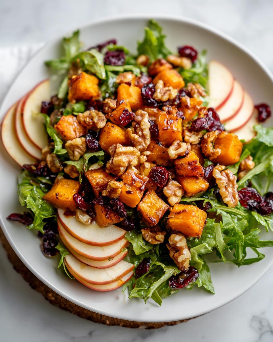 A vibrant fall harvest salad featuring roasted butternut squash cubes, walnuts, dried cranberries, and apple slices over mixed greens.