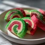 Close-up of sliced, colorful pinwheel cookies featuring red, white, and green layers coated in sparkling sugar.