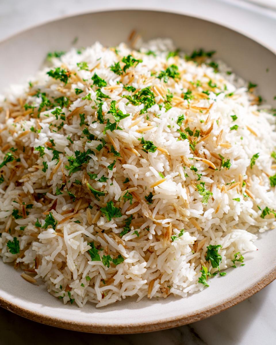 A close-up of fluffy white rice pilaf mixed with toasted vermicelli noodles and topped with fresh chopped parsley.