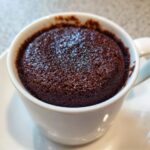 Close-up of a rich, dark chocolate mug cake baked perfectly inside a white ceramic mug.