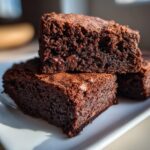 Close-up of stacked, fudgy date brownies showing a rich, dark interior and melted chocolate chips.