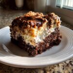 A rich slice of german chocolate poke cake showing the dark chocolate base, white filling, and coconut-pecan topping.
