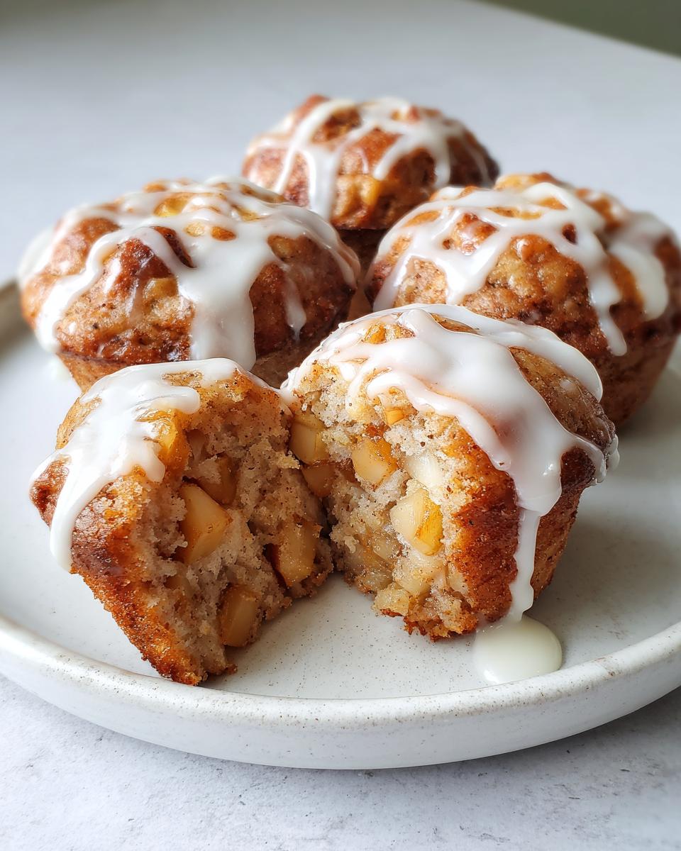 A close-up of several baked apple fritters topped with white glaze, one split open revealing chunks of apple inside.