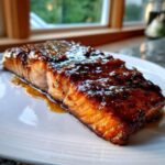 Close-up of a perfectly cooked salmon fillet covered in a rich, dark glaze, served on a white plate.