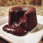 A perfect chocolate lava cake cut open, revealing a rich, molten center oozing onto a white plate.