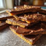 A stack of rich, broken pieces of graham cracker toffee topped with melted chocolate and crumbs.