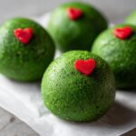 Close-up of several bright green Grinch Oreo Balls, each topped with a small red heart candy.