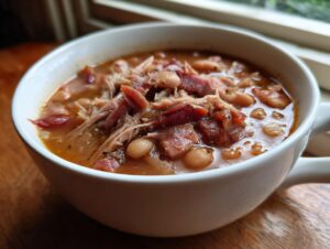 Close-up of a white mug filled with rich, savory ham and bean soup, featuring shredded ham and white beans.