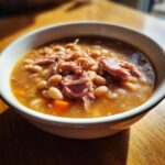 A close-up of a white bowl filled with rich Ham and bean soup, featuring white beans and shredded ham.