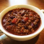 Close-up of a white bowl filled with rich, thick high protein chili featuring ground meat, kidney beans, and tomatoes.