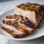 Close-up of a juicy, herb-crusted pork loin roast, sliced to show the tender interior.