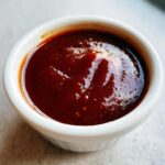 Close-up of thick, glossy, dark red homemade bbq sauce served in a small white dipping bowl.