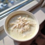 A close-up of a white bowl filled with homemade cream of chicken soup, topped generously with shredded white meat chicken.