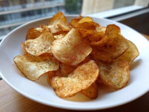 Close-up of a white bowl filled with golden, seasoned, homemade potato chips, highlighting their crunch.