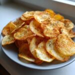 A close-up of a generous pile of homemade, seasoned potato chips dusted with paprika and herbs.