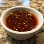 Close-up of homemade teriyaki sauce in a white dipping bowl, showing visible minced garlic pieces.