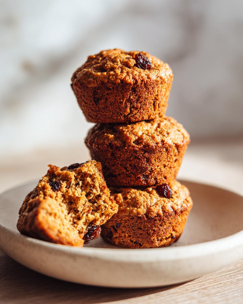 Three stacked honey bran muffins with one broken open showing the texture and raisins inside.