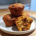 A stack of three golden brown honey bran muffins, one cut in half showing the moist interior filled with raisins.