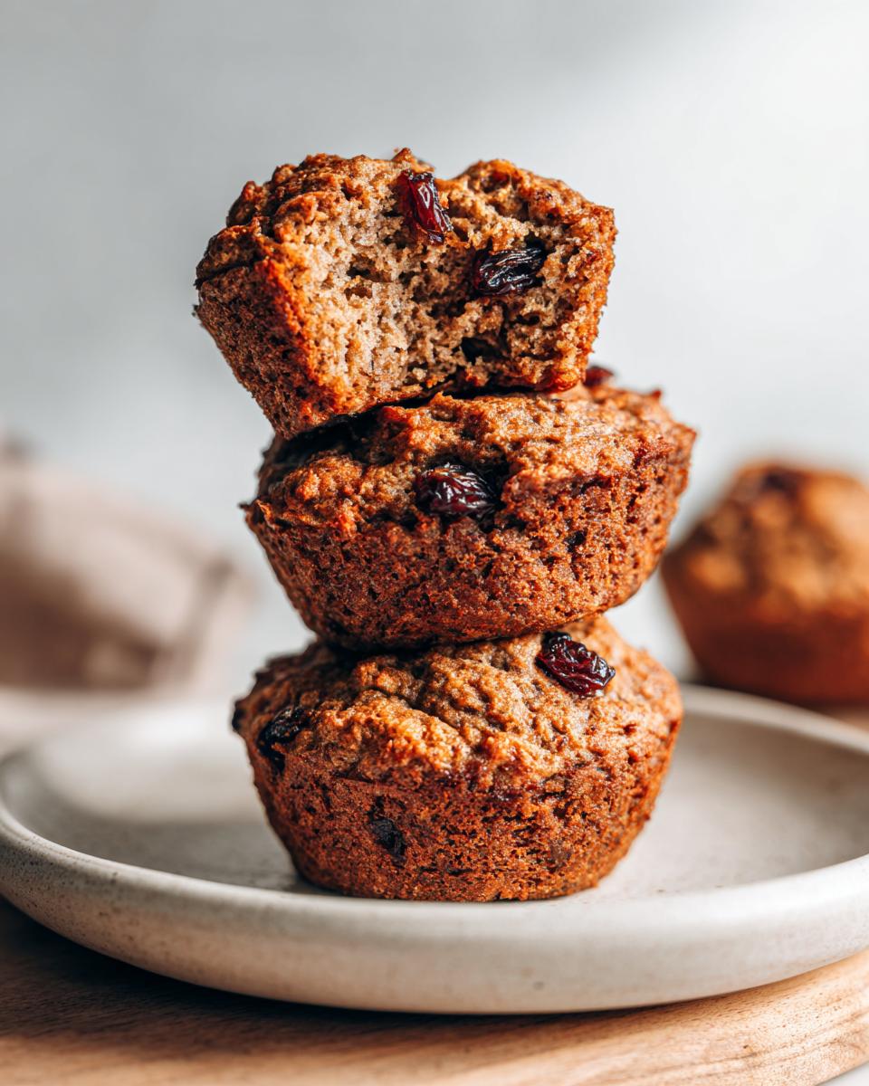 A stack of three moist honey bran muffins, one broken open to show the texture and raisins inside.