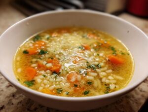 A close-up, featured image of a bowl of warm Italian penicillin soup featuring small pasta, sliced carrots, and parsley garnish.