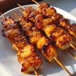 Close-up of several glistening, glazed chicken skewers coated in honey garlic sauce, resting on a white plate.