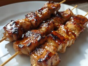 Close-up of three glossy, caramelized honey garlic chicken skewers resting on a white plate.