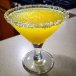 A vibrant yellow lemon drop martini in a coupe glass with a thick, sparkling sugar rim.