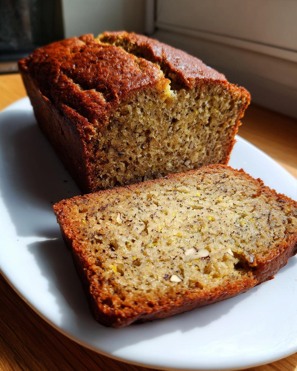A golden-brown loaf of banana zucchini bread sliced on a white plate, showing moist texture and nuts.