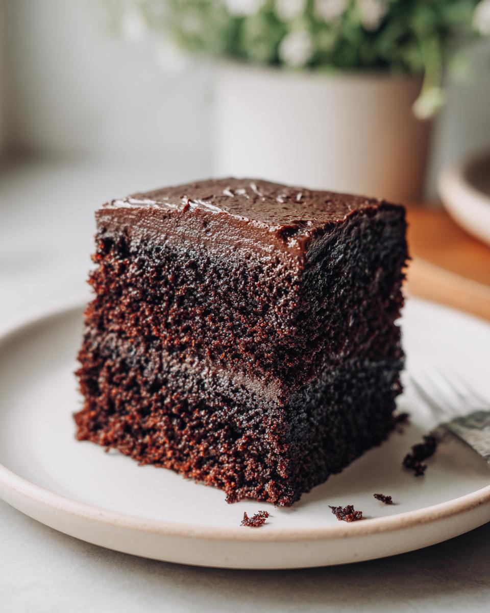 A close-up of a thick slice of moist chocolate cake topped with dark chocolate ganache frosting.