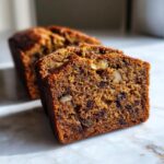 Close-up of two moist slices of date nut bread showing walnuts and dark fruit pieces baked inside.
