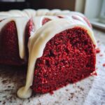 Close-up of a slice of moist red velvet bundt cake topped with dripping white cream cheese glaze.