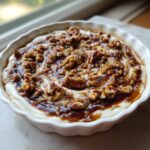 Close-up of a creamy, no-bake pecan pie dip topped with caramel sauce and chopped pecans.