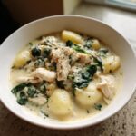 A close-up of a bowl of creamy olive garden chicken gnocchi soup with chunks of chicken, spinach, and potato gnocchi.