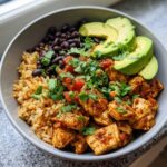 A close-up of a delicious chicken burrito bowl featuring seasoned chicken, rice, black beans, salsa, and sliced avocado.