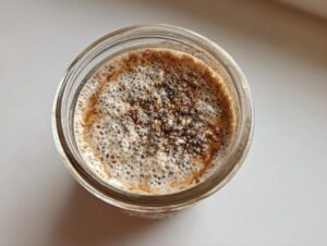 Overhead shot of prepared chia seed pudding in a glass jar, showing soaked chia seeds and a frothy, spiced top layer.