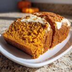 Two thick slices of moist pumpkin cream cheese bread with a visible cream cheese swirl on top, served on a white plate.