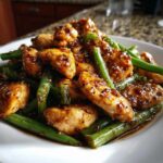 Close-up of glossy, saucy chicken and green beans stir-fry, highlighting the glaze on the chicken and green beans.