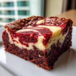 A close-up of a rich, fudgy red velvet cheesecake brownies square with a beautiful red and cream swirl topping.