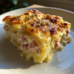 A close-up slice of rich, creamy scalloped potatoes and ham with a golden, cheesy, baked top.
