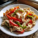 Shredded chicken mixed with colorful sliced bell peppers and onions, ready for crockpot chicken fajitas.