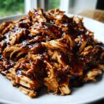 Close-up of moist, shredded crockpot teriyaki chicken generously coated in a thick, glossy teriyaki sauce.
