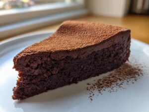 A decadent slice of flourless chocolate torte, dusted heavily with cocoa powder, sitting on a white plate.